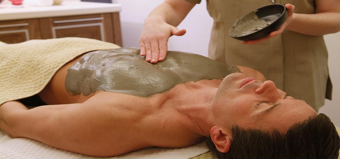 Terapeuta aplicando una envoltura de arcilla sobre el torso de un cliente