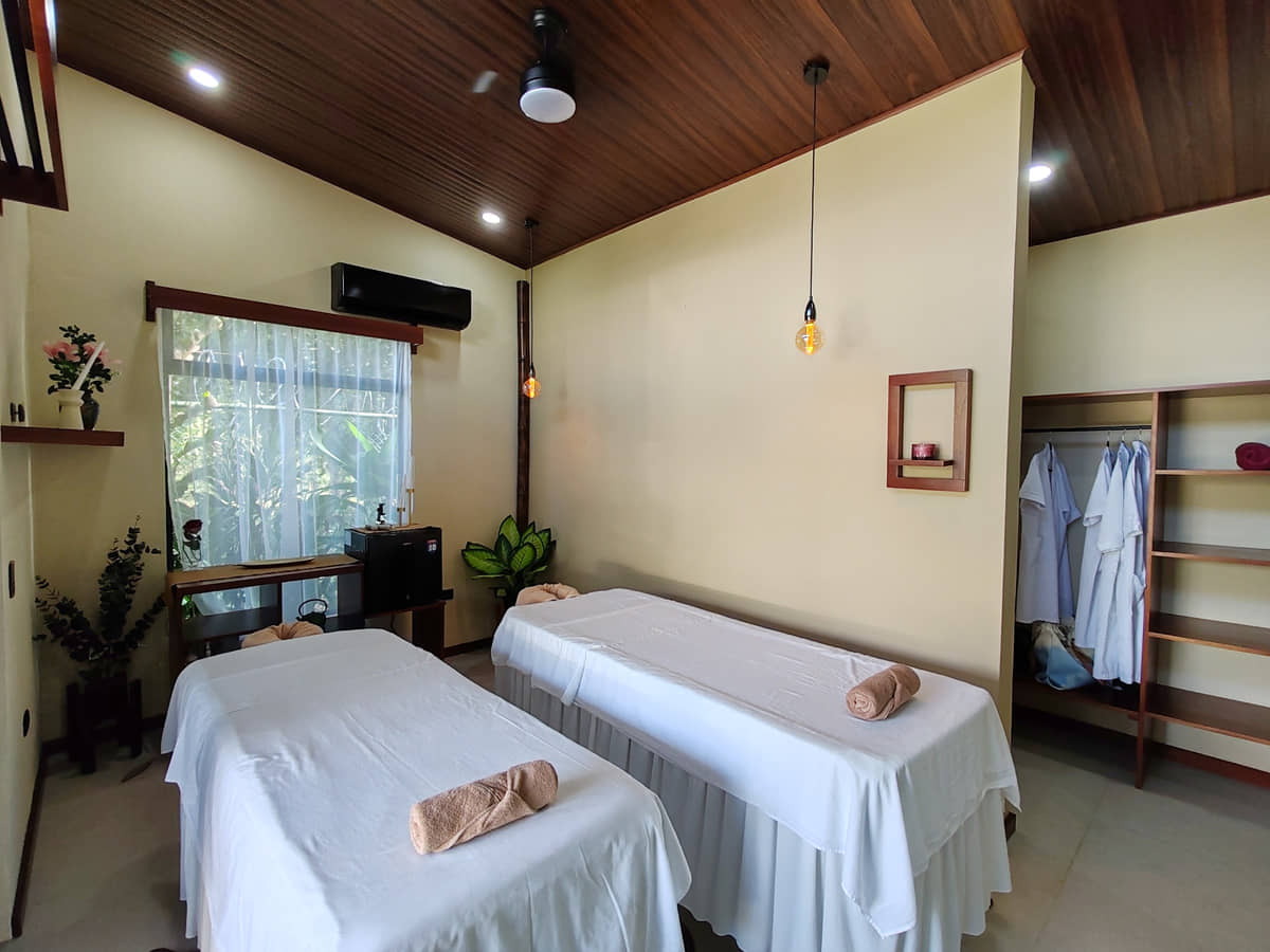 La sala de dos camillas de Reborn Spa: techo de madera, ventana al jardín y batas colgadas